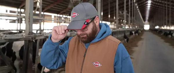 Photo of a man in a KUHN hat and vest standing in a dairy barn